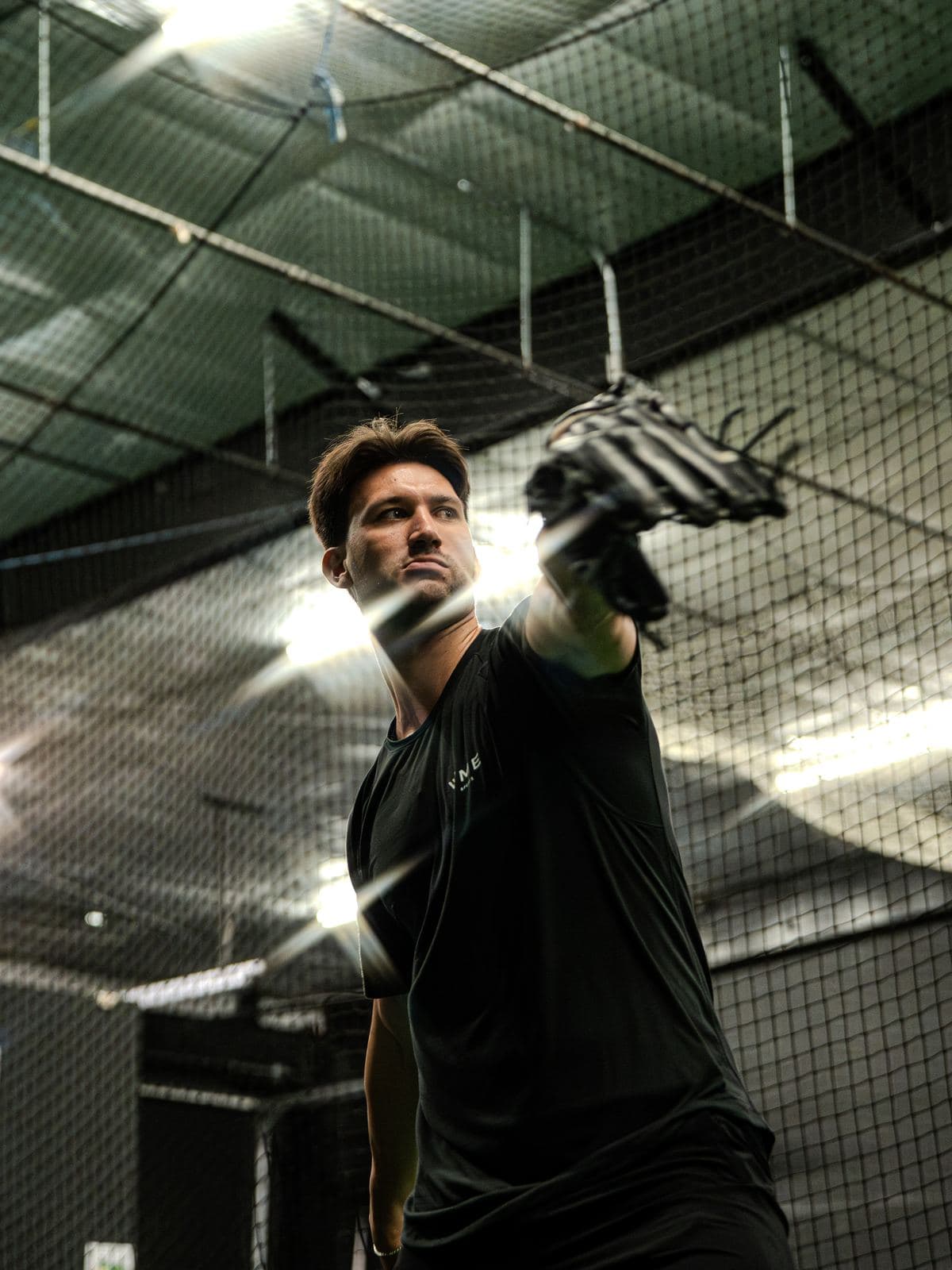 A PPL athlete at release in the cage, glove arm extended, cage lights behind him