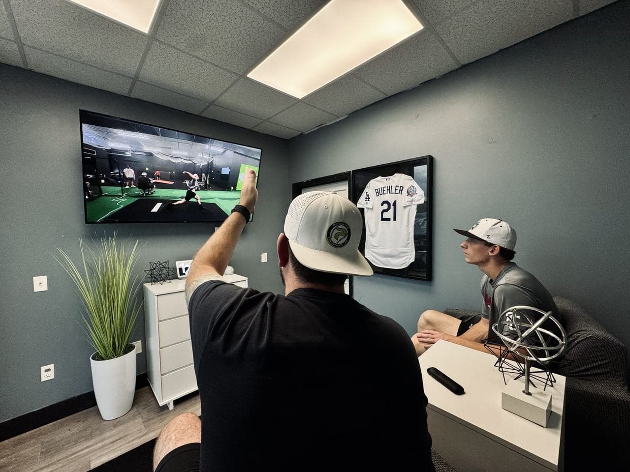 A PPL coach pointing at a delivery on the review room TV while an athlete watches