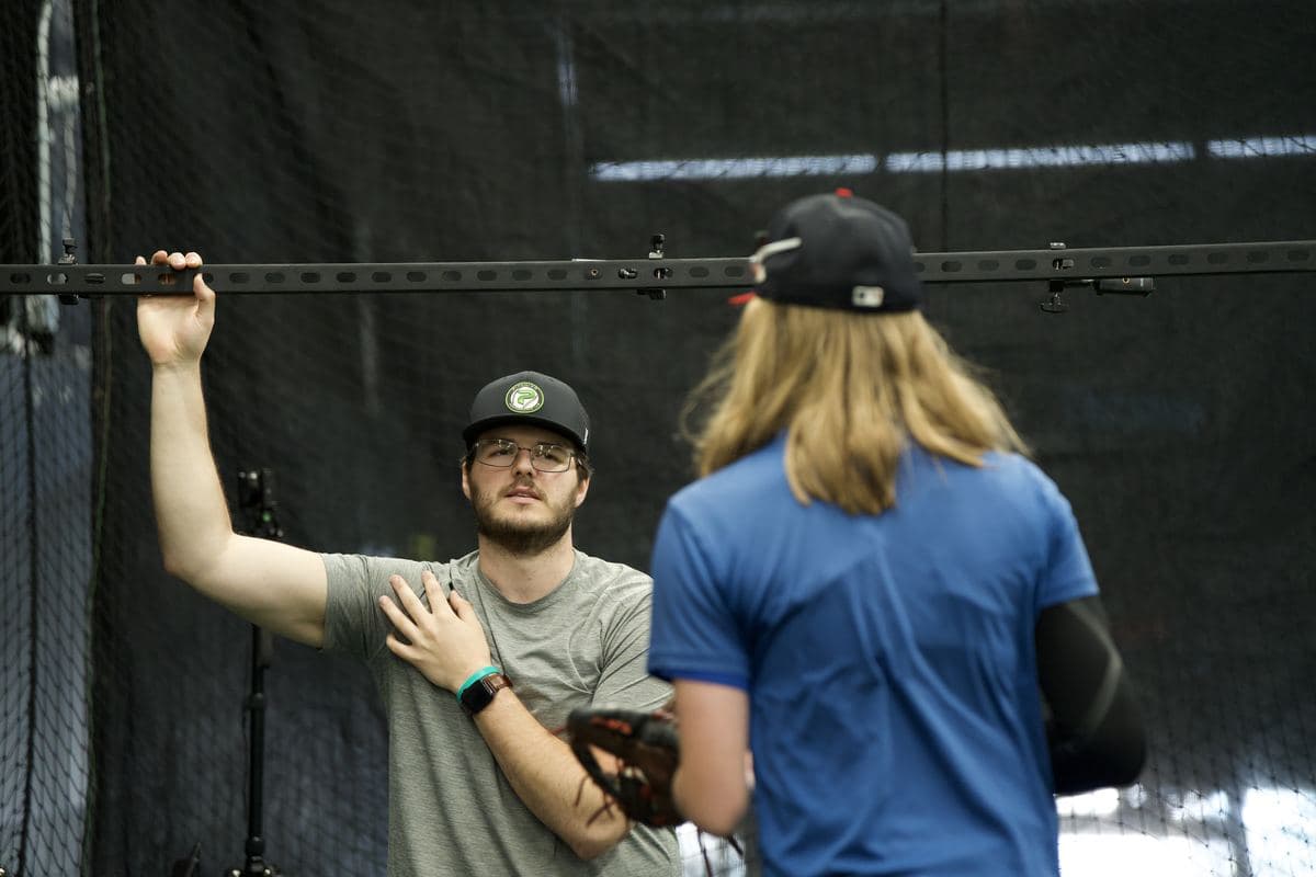 A PPL coach demonstrating an arm position to an athlete in the cage