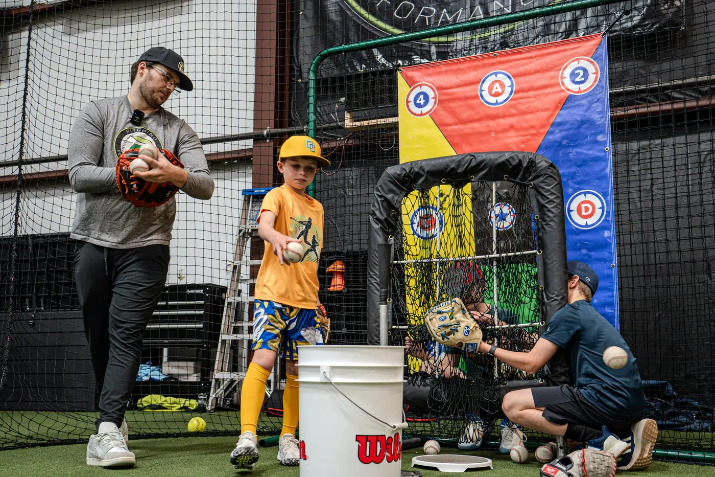 A coach flipping a ball to a young Academy player beside the target net